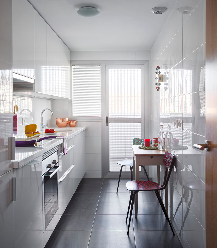 Small eclectic single-wall eat-in kitchen in Malaga with an undermount sink, flat-panel cabinets, white cabinets, white splashback, stainless steel appliances, slate floors, solid surface benchtops and no island.