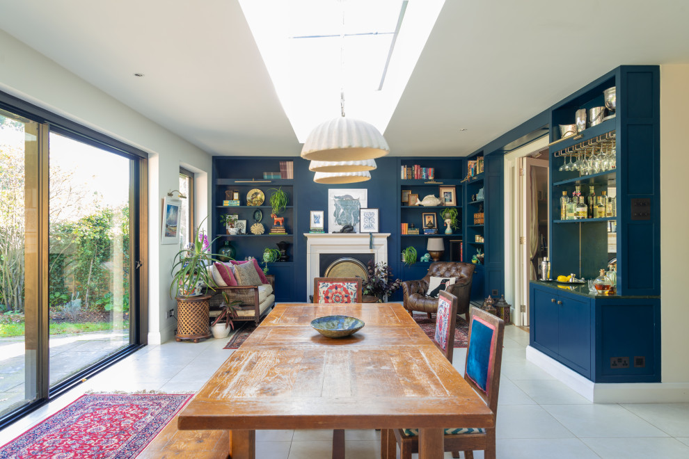 Idée de décoration pour une grande salle à manger ouverte sur le salon bohème avec un mur bleu, un sol en carrelage de porcelaine, une cheminée standard, un manteau de cheminée en plâtre, un sol beige et éclairage.