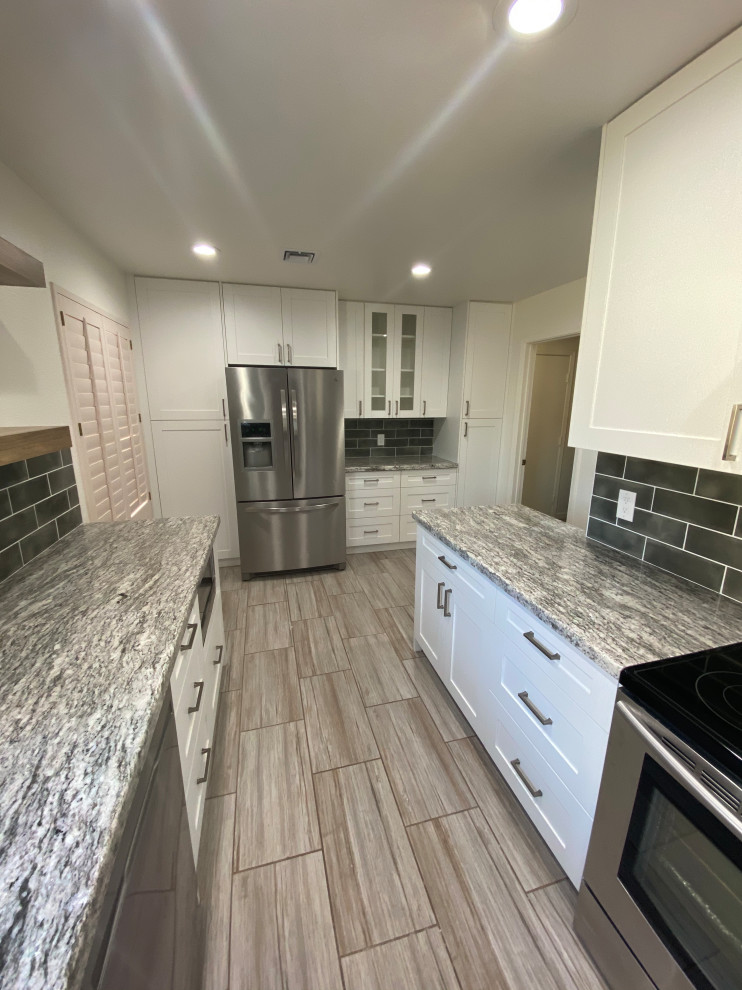 This is an example of a mid-sized modern galley kitchen pantry in Phoenix with a farmhouse sink, shaker cabinets, white cabinets, granite benchtops, brown splashback, ceramic splashback, stainless steel appliances, ceramic floors, no island, grey floor, grey benchtop and vaulted.