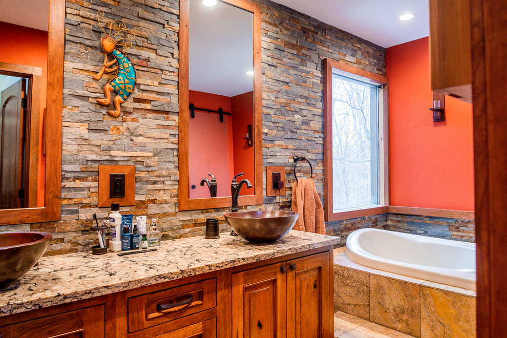 This is an example of a country master bathroom in Other with raised-panel cabinets, medium wood cabinets, a drop-in tub, stone tile, orange walls, a vessel sink, beige floor and multi-coloured benchtops.