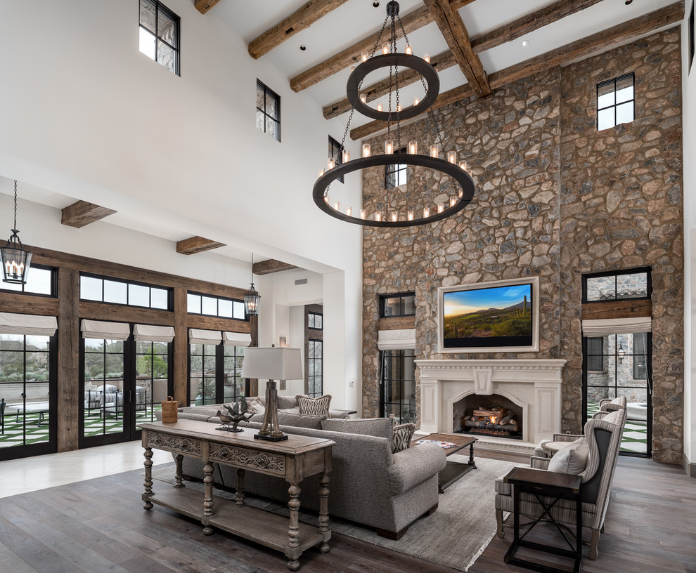 Design ideas for an expansive open concept living room in Phoenix with multi-coloured walls, dark hardwood floors, a standard fireplace, a stone fireplace surround, a wall-mounted tv and brown floor.