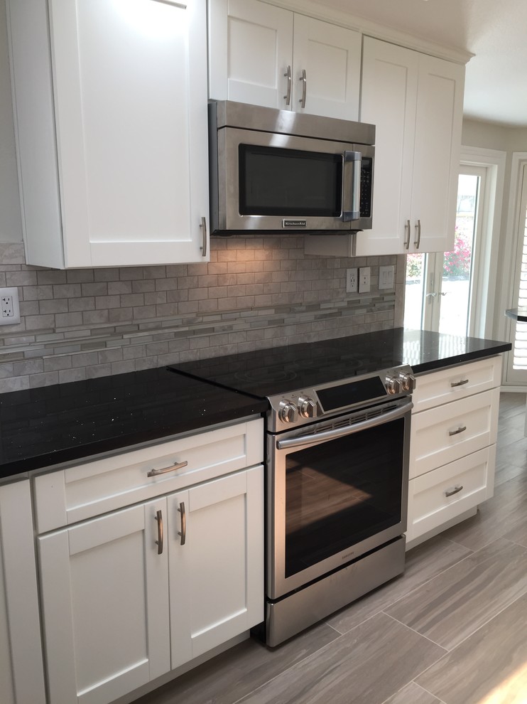 Photo of a mid-sized contemporary u-shaped eat-in kitchen in Los Angeles with an undermount sink, shaker cabinets, white cabinets, quartz benchtops, grey splashback, mosaic tile splashback, stainless steel appliances, porcelain floors and with island.