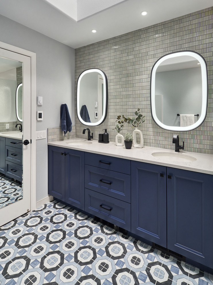 This is an example of a mid-sized transitional master bathroom in Portland with recessed-panel cabinets, blue cabinets, a corner shower, a one-piece toilet, gray tile, ceramic tile, white walls, ceramic floors, an undermount sink, engineered quartz benchtops, blue floor, a hinged shower door, grey benchtops, a shower seat, a double vanity, a built-in vanity and recessed.