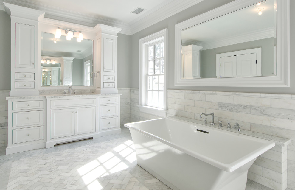 Expansive contemporary master bathroom in New York with an undermount sink, white cabinets, marble benchtops, a freestanding tub, gray tile, stone tile, grey walls and marble floors.