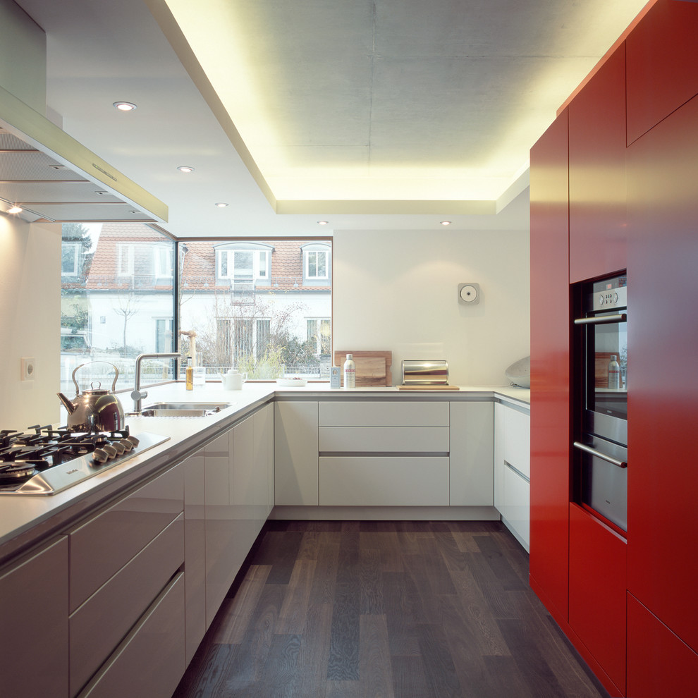 This is an example of a mid-sized contemporary u-shaped separate kitchen in Munich with a double-bowl sink, flat-panel cabinets, red cabinets, stainless steel appliances and dark hardwood floors.