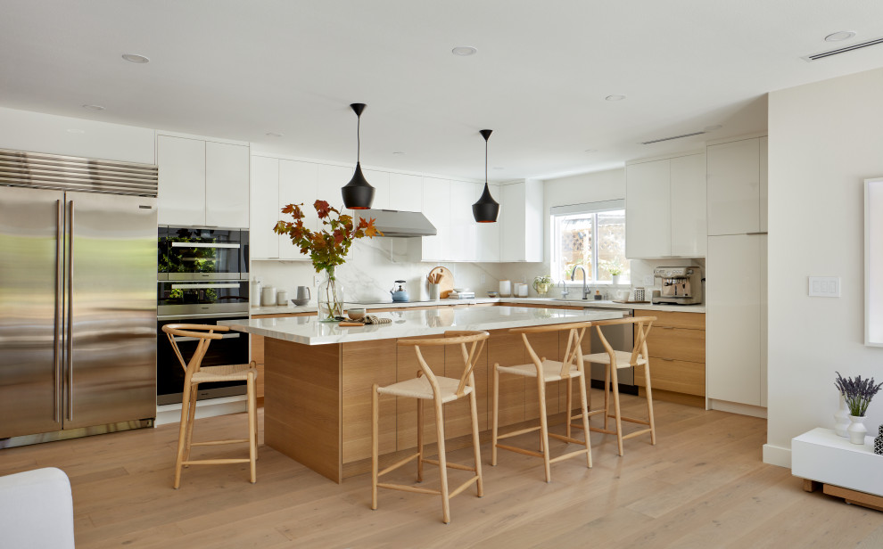 Photo of a large midcentury l-shaped eat-in kitchen in San Francisco with an undermount sink, flat-panel cabinets, brown cabinets, quartz benchtops, white splashback, porcelain splashback, stainless steel appliances, light hardwood floors, with island and white benchtop.