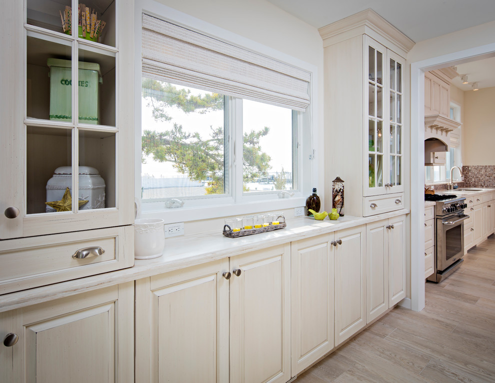 Example of a large transitional porcelain tile kitchen design with an undermount sink, recessed-panel cabinets, solid surface countertops, stainless steel appliances and an island
