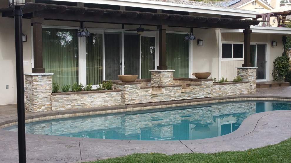Large modern backyard custom-shaped aboveground pool in Los Angeles with a water feature and stamped concrete.