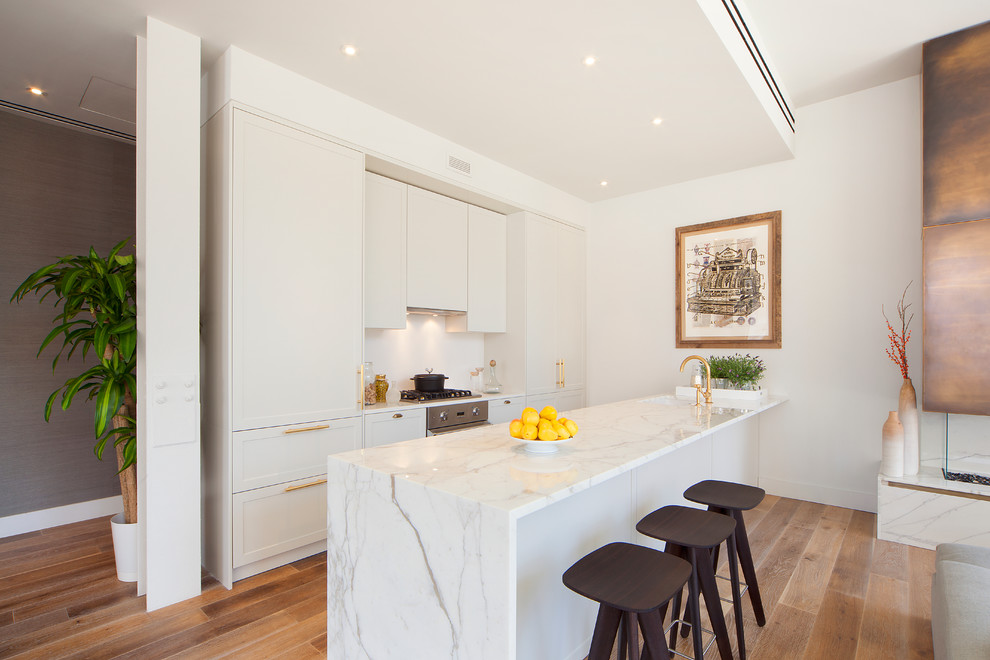 Photo of a mid-sized modern galley open plan kitchen in New York with a single-bowl sink, shaker cabinets, white cabinets, marble benchtops, white splashback, stainless steel appliances, medium hardwood floors and a peninsula.