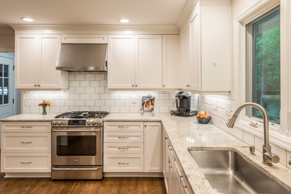 Mid-sized l-shaped eat-in kitchen in Atlanta with a drop-in sink, recessed-panel cabinets, white cabinets, granite benchtops, white splashback, subway tile splashback, stainless steel appliances, medium hardwood floors, a peninsula, brown floor and yellow benchtop.