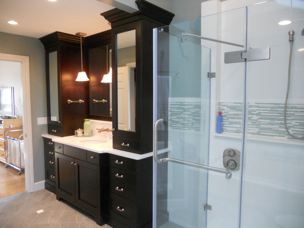 Large transitional master gray tile and stone tile ceramic tile corner bathtub photo with an undermount sink, recessed-panel cabinets, dark wood cabinets, quartz countertops, a two-piece toilet and gray walls