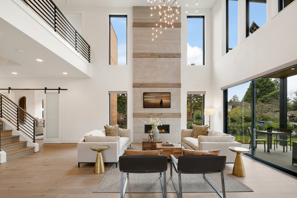 Inspiration for a large contemporary open concept living room in Seattle with white walls, medium hardwood floors, a standard fireplace, a wall-mounted tv, a stone fireplace surround and beige floor.