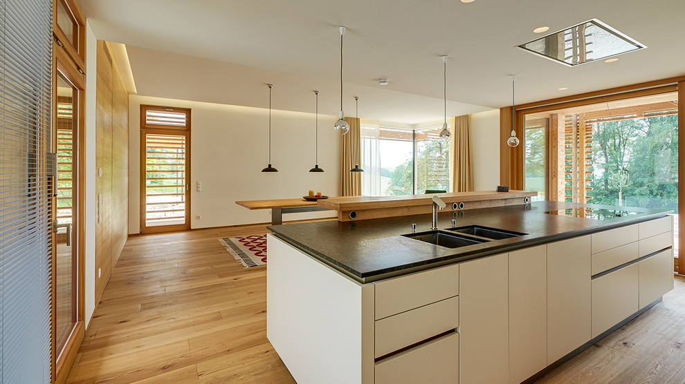 Inspiration for an expansive contemporary eat-in kitchen in Munich with flat-panel cabinets, white cabinets, with island, a double-bowl sink and medium hardwood floors.