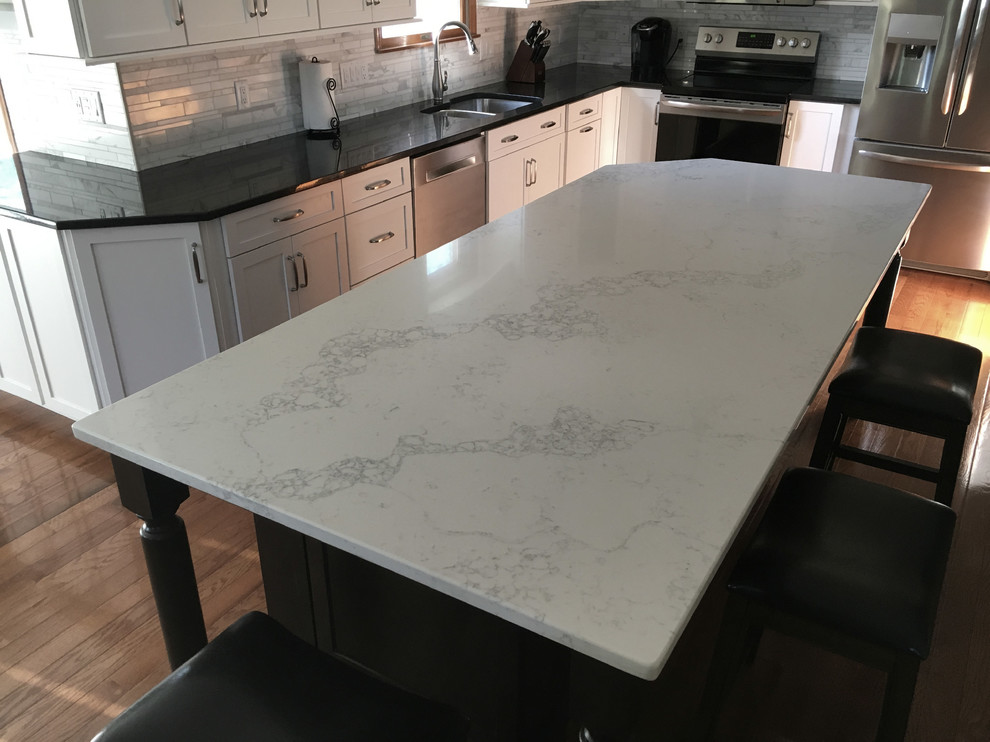 Example of a large transitional single-wall medium tone wood floor eat-in kitchen design with an undermount sink, shaker cabinets, white cabinets, granite countertops, multicolored backsplash, marble backsplash, stainless steel appliances, an island and black countertops