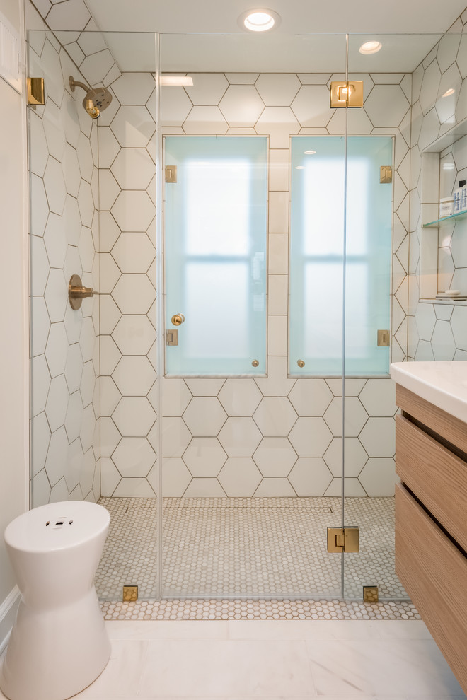 Photo of a small contemporary master bathroom in New York with flat-panel cabinets, light wood cabinets, a curbless shower, a wall-mount toilet, white tile, ceramic tile, white walls, marble floors, an integrated sink, solid surface benchtops, white floor, a hinged shower door and white benchtops.