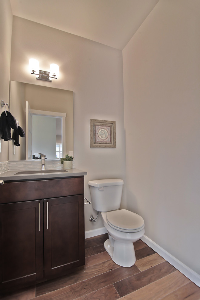 Photo of a small contemporary powder room in Seattle with an undermount sink, shaker cabinets, dark wood cabinets, engineered quartz benchtops, a two-piece toilet, medium hardwood floors and matchstick tile.