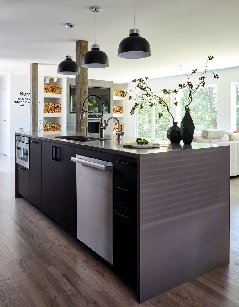 This is an example of a mid-sized contemporary single-wall open plan kitchen in New York with a drop-in sink, flat-panel cabinets, dark wood cabinets, concrete benchtops, black splashback, stone tile splashback, panelled appliances, light hardwood floors, with island, grey floor and grey benchtop.