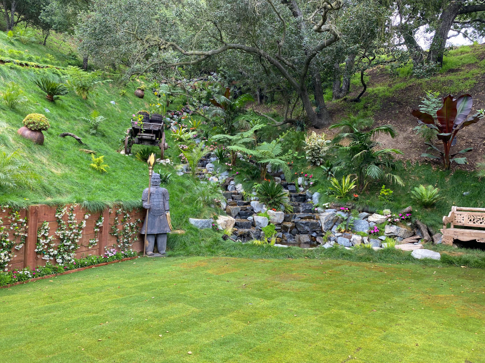 Geometrischer, Großer, Halbschattiger Asiatischer Gartenwasserfall im Sommer, hinter dem Haus mit Flusssteinen in Los Angeles