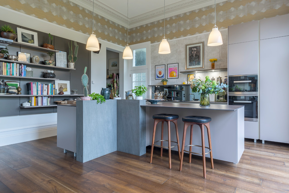 This is an example of a mid-sized eclectic kitchen in Manchester with flat-panel cabinets, grey cabinets, brown floor, grey splashback, black appliances and dark hardwood floors.