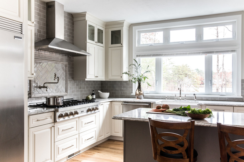 Design ideas for a traditional l-shaped eat-in kitchen in Boston with a farmhouse sink, raised-panel cabinets, white cabinets, grey splashback, subway tile splashback, stainless steel appliances, medium hardwood floors, with island, brown floor and grey benchtop.