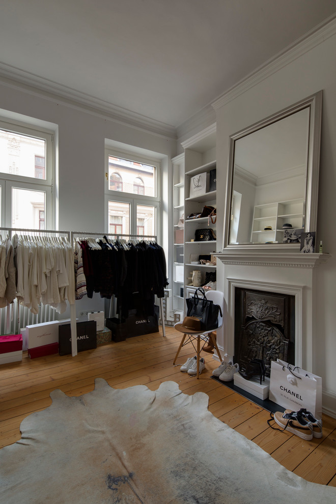 This is an example of a mid-sized industrial women's dressing room in Cologne with open cabinets, white cabinets, light hardwood floors and beige floor.