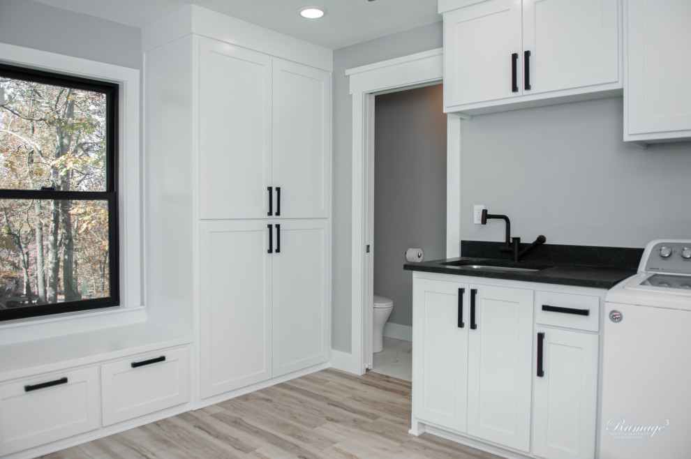 Inspiration for a mid-sized transitional single-wall dedicated laundry room in Other with an undermount sink, recessed-panel cabinets, white cabinets, granite benchtops, grey walls, vinyl floors, a side-by-side washer and dryer, beige floor and black benchtop.
