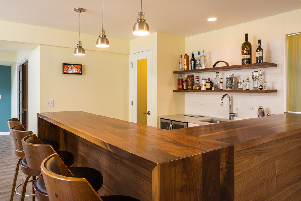 This is an example of an expansive midcentury u-shaped seated home bar in Detroit with an undermount sink, wood benchtops, white splashback, subway tile splashback, brown floor and vinyl floors.