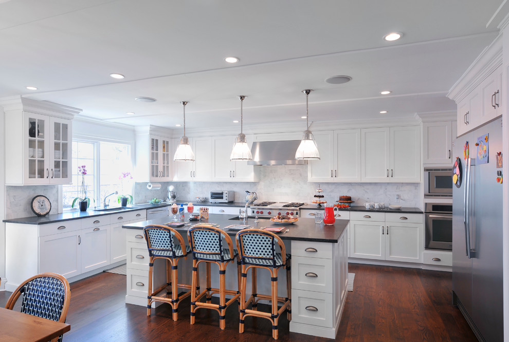 This is an example of a large traditional l-shaped eat-in kitchen in New York with shaker cabinets, stainless steel appliances, white cabinets, white splashback, stone slab splashback, dark hardwood floors, with island and an undermount sink.