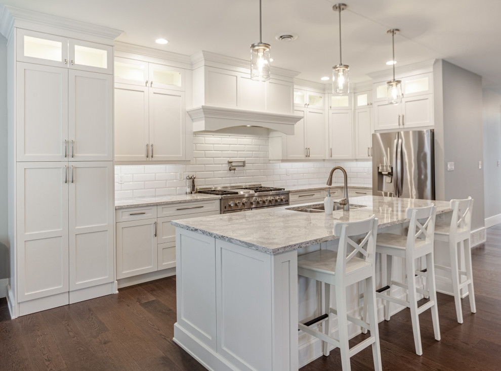 Mid-sized traditional l-shaped open plan kitchen in Vancouver with an undermount sink, shaker cabinets, white cabinets, quartz benchtops, white splashback, ceramic splashback, stainless steel appliances, dark hardwood floors, with island, brown floor and beige benchtop.