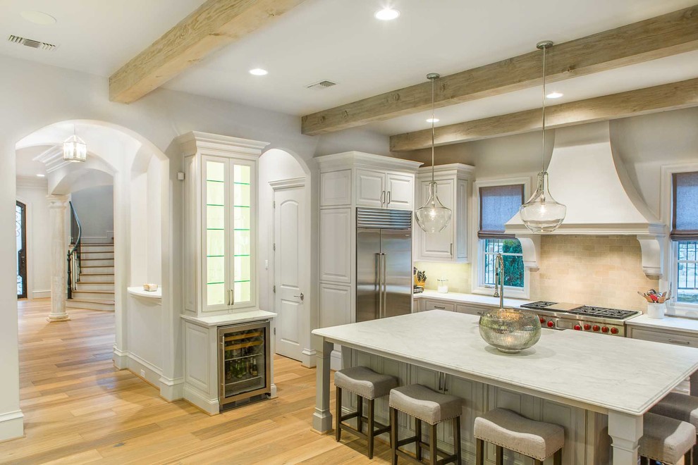 Inspiration for a large transitional single-wall light wood floor open concept kitchen remodel in Dallas with recessed-panel cabinets, white cabinets, marble countertops, beige backsplash, stone tile backsplash, stainless steel appliances and an island