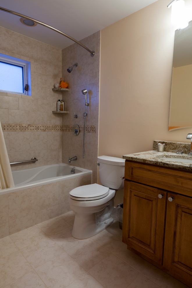 This is an example of a mid-sized transitional bathroom in Bridgeport with an undermount sink, raised-panel cabinets, medium wood cabinets, granite benchtops, an alcove tub, a shower/bathtub combo, a two-piece toilet, beige tile, porcelain tile, beige walls and porcelain floors.