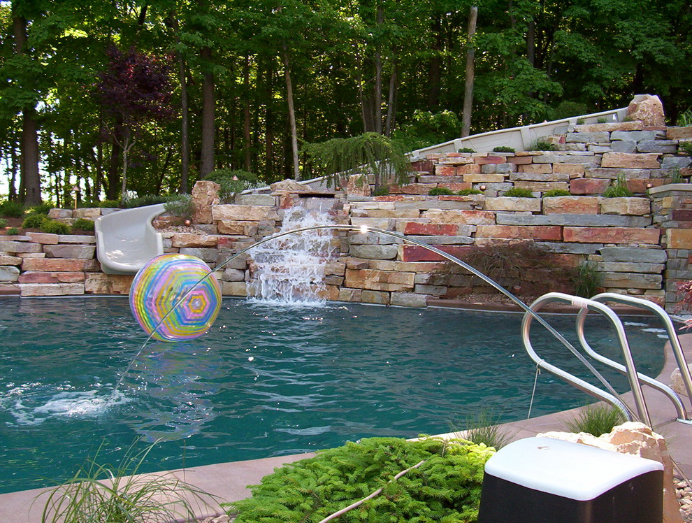 Large traditional backyard pool in Grand Rapids with a water slide and stamped concrete.