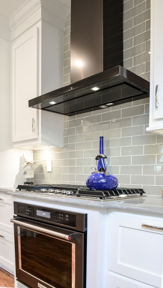 Inspiration for a mid-sized transitional l-shaped open plan kitchen in Charlotte with an undermount sink, shaker cabinets, white cabinets, granite benchtops, grey splashback, glass tile splashback, stainless steel appliances, medium hardwood floors and with island.