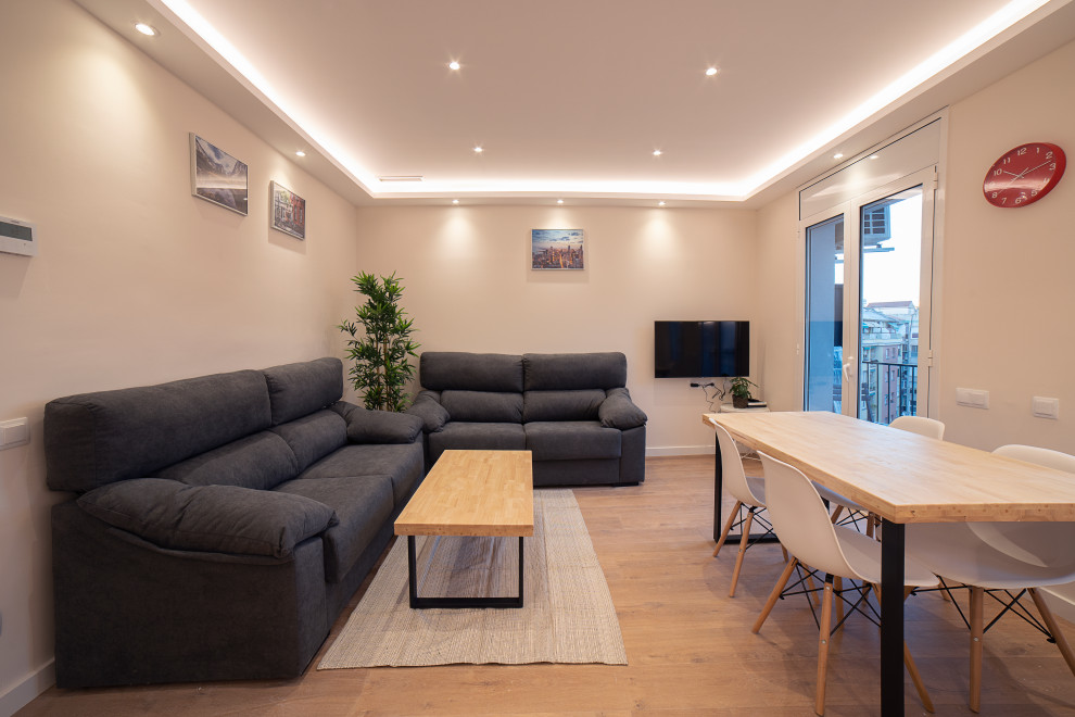 This is an example of a medium sized contemporary open plan living room in Barcelona with beige walls, medium hardwood flooring, no fireplace, a wall mounted tv and brown floors.