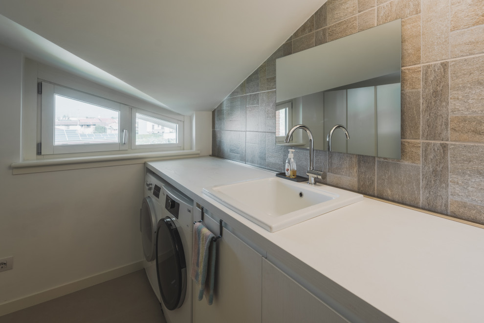 This is an example of a mid-sized industrial galley dedicated laundry room in Milan with a drop-in sink, flat-panel cabinets, yellow cabinets, laminate benchtops, beige splashback, ceramic splashback, white walls, porcelain floors, a side-by-side washer and dryer, beige floor and white benchtop.