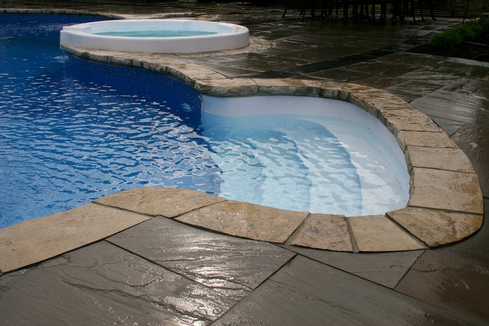 Design ideas for a mid-sized contemporary backyard custom-shaped natural pool in Toronto with a hot tub and natural stone pavers.