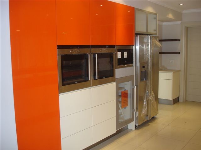 Photo of a traditional u-shaped kitchen in Other with a double-bowl sink, flat-panel cabinets, white cabinets, solid surface benchtops, brown splashback, glass sheet splashback, stainless steel appliances, light hardwood floors and with island.