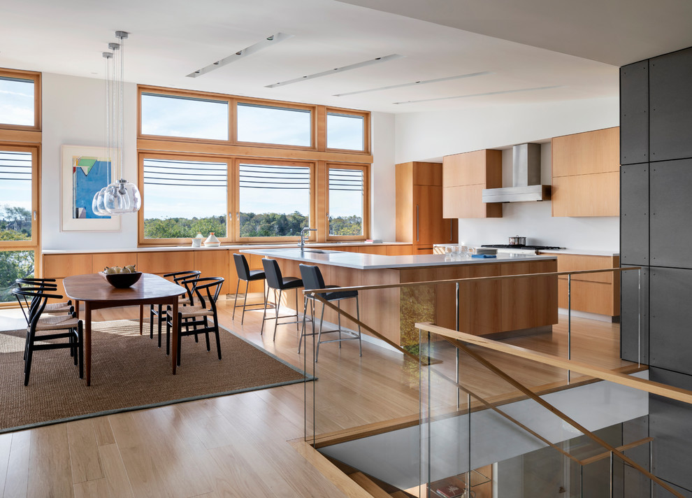 This is an example of a mid-sized modern kitchen in Providence with an undermount sink, flat-panel cabinets, medium wood cabinets, solid surface benchtops, white splashback, panelled appliances, light hardwood floors, with island and white benchtop.