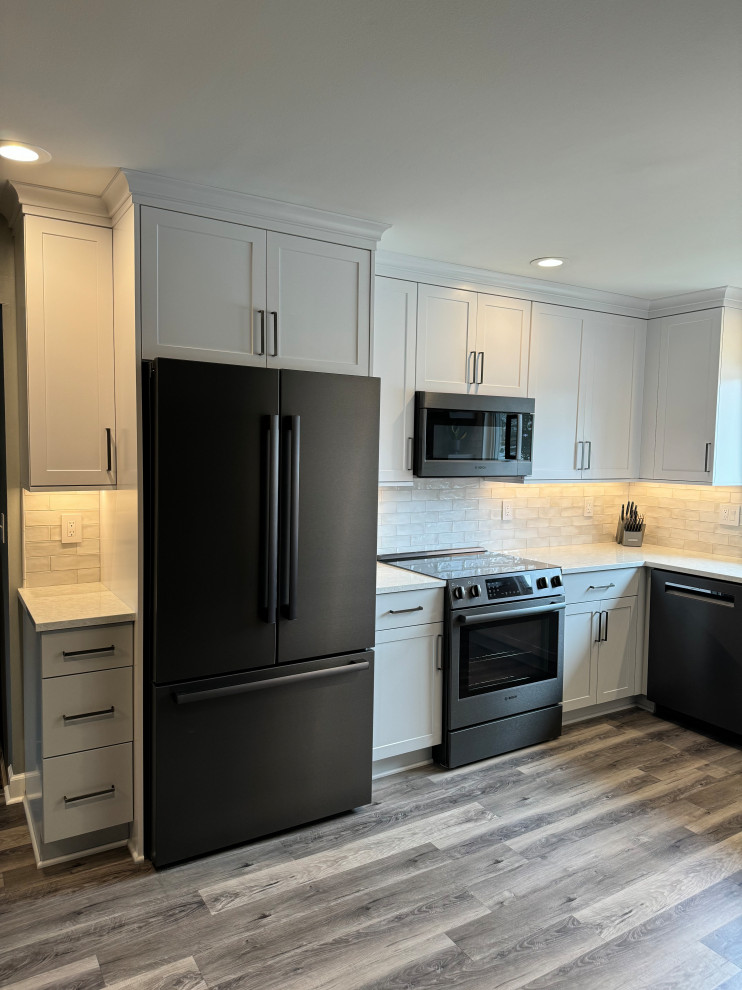 Photo of a medium sized classic u-shaped kitchen/diner in Detroit with a single-bowl sink, shaker cabinets, white cabinets, engineered stone countertops, white splashback, ceramic splashback, black appliances, vinyl flooring, no island, brown floors and white worktops.