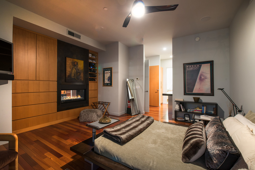 Contemporary bedroom in Minneapolis with grey walls, medium hardwood floors, a two-sided fireplace and brown floor.