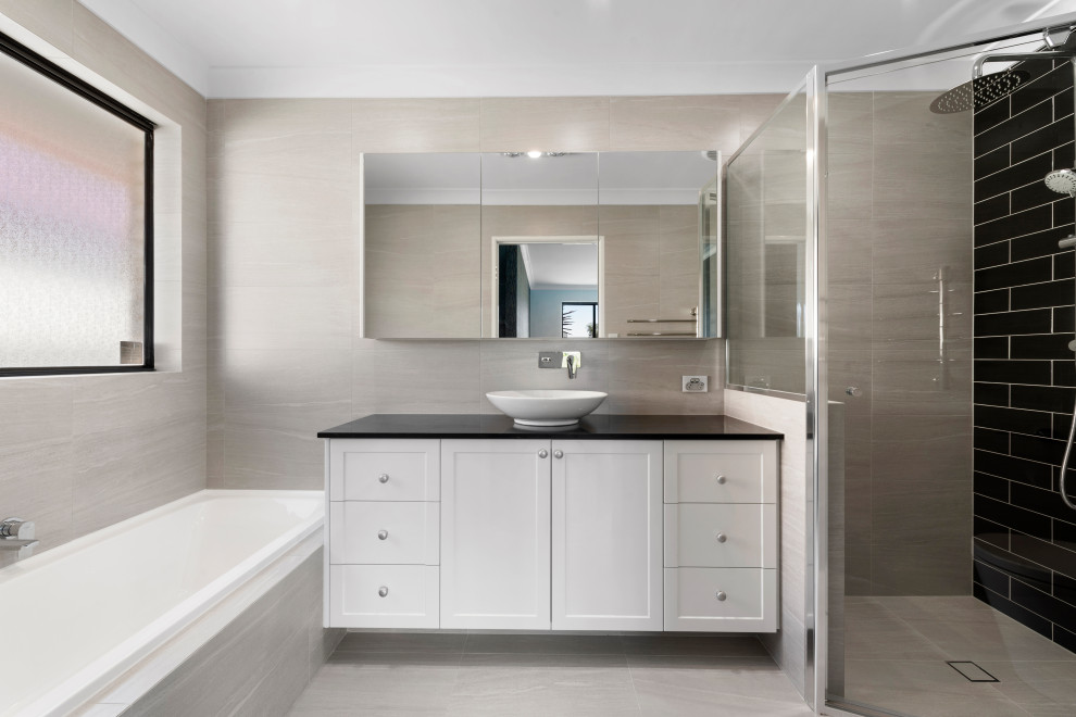 Design ideas for a mid-sized modern master bathroom in Perth with recessed-panel cabinets, white cabinets, a drop-in tub, a corner shower, a one-piece toilet, black tile, subway tile, beige walls, a vessel sink, solid surface benchtops, beige floor, a hinged shower door and black benchtops.