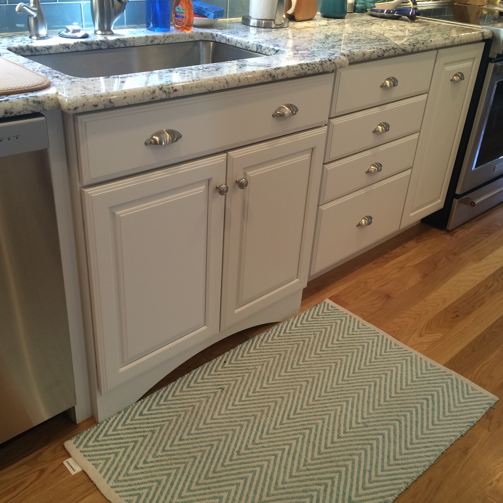 Transitional u-shaped medium tone wood floor eat-in kitchen photo in Boston with an undermount sink, raised-panel cabinets, white cabinets, granite countertops, blue backsplash, glass tile backsplash, stainless steel appliances and an island