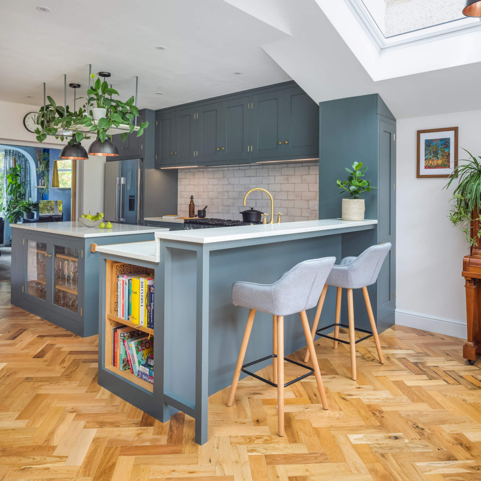 Large contemporary l-shaped open plan kitchen in London with shaker cabinets, grey cabinets, with island and white benchtop.
