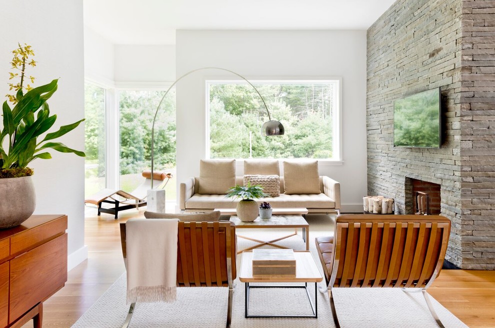 Photo of a contemporary open concept family room in New York with white walls, medium hardwood floors, a standard fireplace, a stone fireplace surround, a wall-mounted tv and beige floor.