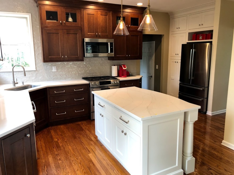 This is an example of a mid-sized traditional l-shaped kitchen pantry in New York with an undermount sink, dark wood cabinets, quartz benchtops, beige splashback, ceramic splashback, stainless steel appliances, medium hardwood floors, with island and white benchtop.