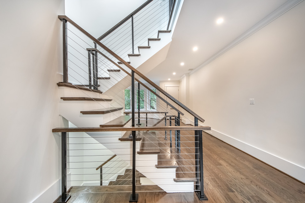 Стильный дизайн: огромная п-образная лестница в современном стиле с деревянными ступенями, крашенными деревянными подступенками и перилами из тросов - последний тренд