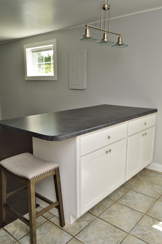 This is an example of a small transitional l-shaped open plan kitchen in Chicago with a drop-in sink, shaker cabinets, white cabinets, laminate benchtops, ceramic floors, with island, multi-coloured floor and grey benchtop.
