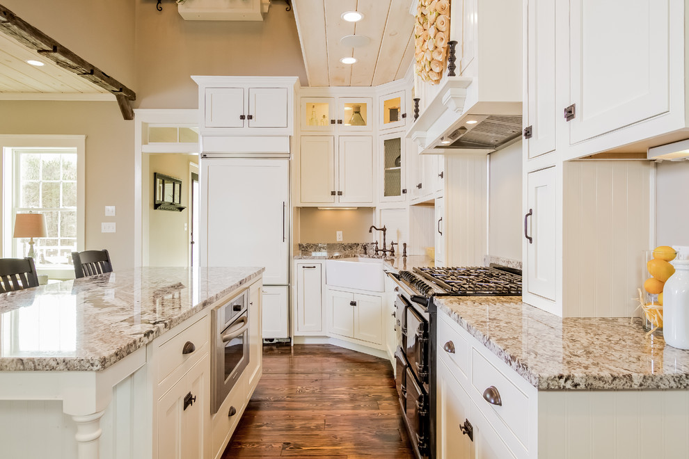 This is an example of a large country u-shaped eat-in kitchen in Boston with a farmhouse sink, beaded inset cabinets, white cabinets, granite benchtops, white appliances, dark hardwood floors and with island.
