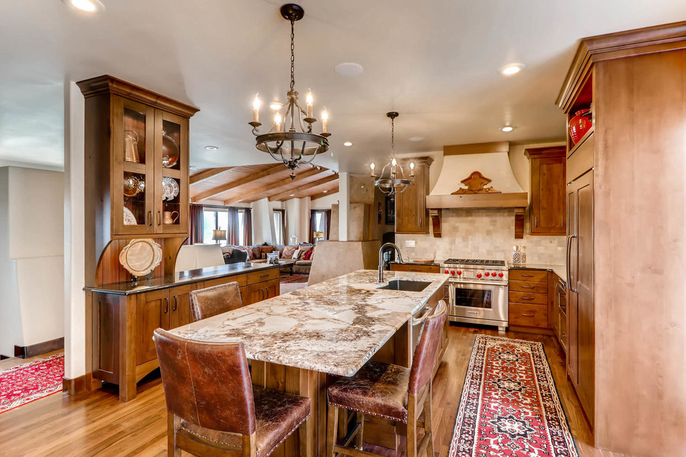 Photo of a large country kitchen in Denver with an undermount sink, flat-panel cabinets, dark wood cabinets, granite benchtops, beige splashback, mosaic tile splashback, stainless steel appliances, medium hardwood floors and with island.