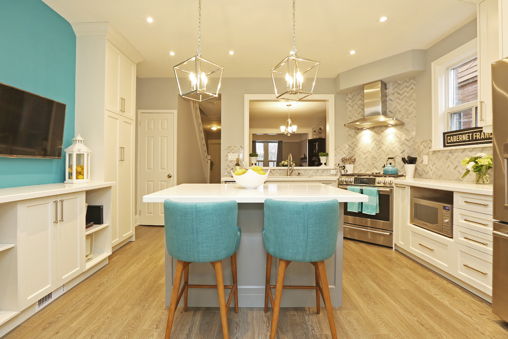 Mid-sized transitional u-shaped light wood floor and brown floor enclosed kitchen photo in Toronto with shaker cabinets, white cabinets, an island, white countertops, an undermount sink, stainless steel appliances, solid surface countertops and gray backsplash